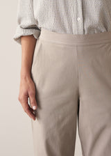 Woman wearing taupe slim fit tapered leg trousers with pale check shirt