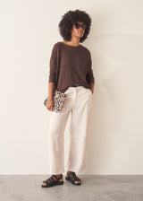 A woman wearing a chocolate brown, fine knit sweater and light cream trousers.