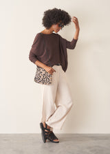 A woman wearing a chocolate brown, fine knit sweater and light cream trousers.