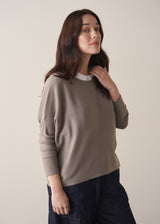 Woman wearing long sleeve stone-grey fine knit sweater with dark blue denim trousers