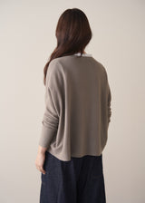 Woman wearing long sleeve stone-grey fine knit sweater with dark blue denim trousers