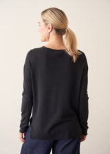 Woman wearing black lightweight knit sweater with blue jeans and a beige jacket