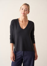 Woman wearing black lightweight knit sweater with blue jeans and a beige jacket