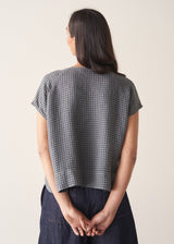 Woman wearing a blue and green check linen top and denim cullottes against a plain background