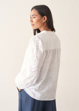 Woman wearing white broderie anglaise long sleeve top and blue linen trousers