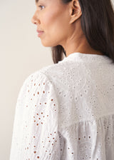 Woman wearing white broderie anglaise long sleeve top and blue linen trousers