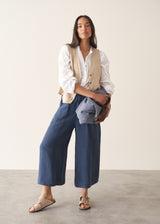 Woman wearing white broderie anglaise long sleeve top and blue linen trousers