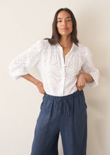 Woman wearing white broderie anglaise long sleeve top and blue linen trousers
