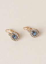 Drop earrings with diamante crystals surrounding a deep navy blue central crystal, on a beige backdrop
