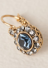 Close up of a drop earring with diamante crystals surrounding a deep navy blue central crystal, on a beige backdrop