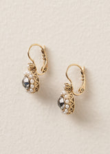Side view of pair of vintage style gold drop earrings with pearls surrounding a smokey grey crystal, on a beige background