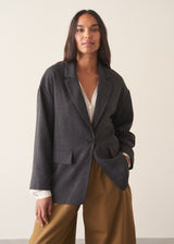 A woman wearing a dark charcoal textured blazer with olive barrel leg trousers and a white blouse