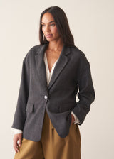 A woman wearing a dark charcoal textured blazer with olive barrel leg trousers and a white blouse