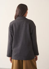 A woman wearing a dark charcoal textured blazer with olive barrel leg trousers and a white blouse