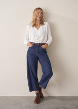 Woman wearing blue barrel leg jeans with a white cotton embroidered top.