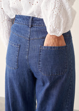 Close-up back view of a person wearing blue denim jeans with a white eyelet blouse, one hand in the back pocket.