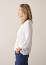 Woman wearing a white lightweight cotton blouse with long sleeves and blue barrel leg jeans