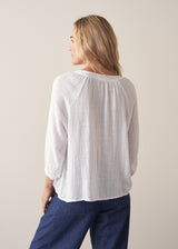 Woman wearing a white lightweight cotton blouse with long sleeves and blue barrel leg jeans