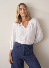 Woman wearing a white lightweight cotton blouse with long sleeves and blue barrel leg jeans