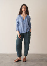 Woman wearing cornflower blue cotton blouse with dark teal linen trousers