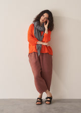 Woman wearing a bright orange cotton blouse and linen trousers against a plain background