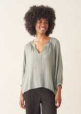 Woman wearing pale green cotton top with black linen trousers.