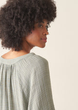 Woman wearing pale green cotton top with black linen trousers.