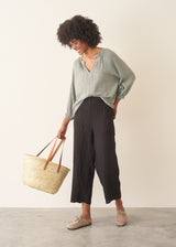 Woman wearing pale green cotton top with black linen trousers.