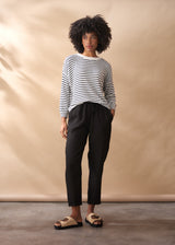 Woman wearing a light knit stripe crew neck sweater with black trousers, on a neutral background