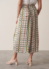 Woman wearing silk blend wide-leg trousers in check print with a sleeveless satin top and strappy sandals, against a beige background