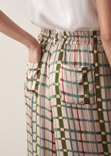 Woman wearing silk blend wide-leg trousers in check print with a sleeveless satin top against a beige background