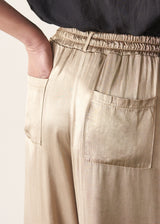 Woman wearing taupe satin wide leg trousers with a black shirt and black sandals