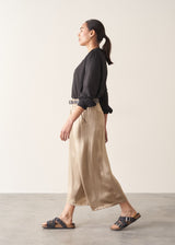 Woman wearing taupe satin wide leg trousers with a black shirt and black sandals