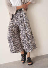 A woman wearing wide-leg leopard print trousers and a white vest top.