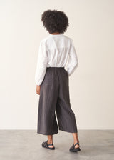 Woman wearing charcoal black stripe wide leg cropped trousers with a white broderie shirt.