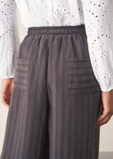 Woman wearing charcoal black stripe wide leg cropped trousers with a white broderie shirt.