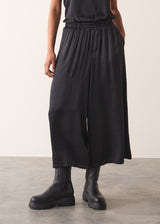 Woman wearing black satin wide leg cropped trousers against a plain background