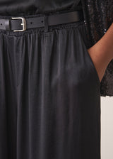 Woman wearing black satin wide leg cropped trousers against a plain background