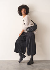 Woman wearing black satin wide leg cropped trousers against a plain background