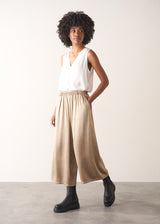 Woman wearing a white sleeveless top and champagne satin wide-leg trousers against a plain background