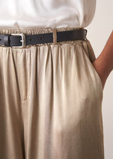 Woman wearing a white sleeveless top and champagne satin wide-leg trousers against a plain background