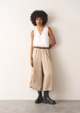 Woman wearing a white sleeveless top and champagne satin wide-leg trousers against a plain background