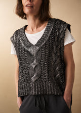 Woman wears a dark grey silver metallic cable knit vest, white short sleeve t-shirt and black jersey drawstring trousers