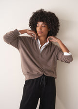 Woman wearing a light brown long-sleeve polo neck sweater and black drawstring trousers against a plain background