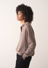 Woman wearing a light brown long-sleeve polo neck sweater and black drawstring trousers against a plain background