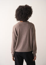 Woman wearing a light brown long-sleeve polo neck sweater and black drawstring trousers against a plain background