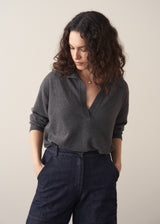 Woman wearing a dark grey polo neck collared jumper and denim wide leg jeans against a beige background
