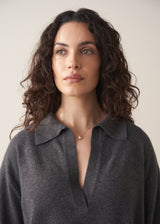 Woman wearing a dark grey polo neck collared jumper and denim wide leg jeans against a beige background