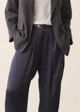A woman wearing dark blue satin trousers with a pale grey blouse and a dark grey blazer