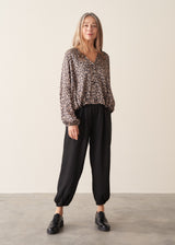 A woman wearing a satin leopard print blouse with a bubble hem and black trousers.